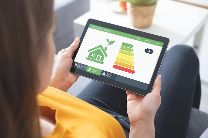 A woman holding a tablet with a smart green house on it.