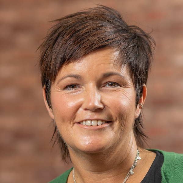 A woman with short hair smiling in front of a brick wall.