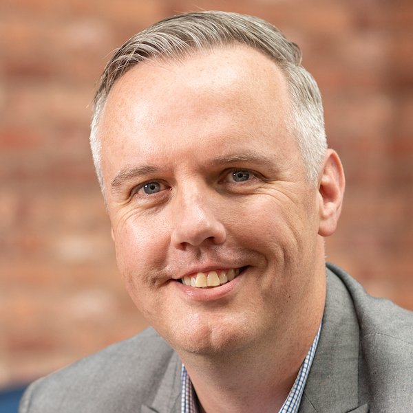 A man in a grey suit smiling.