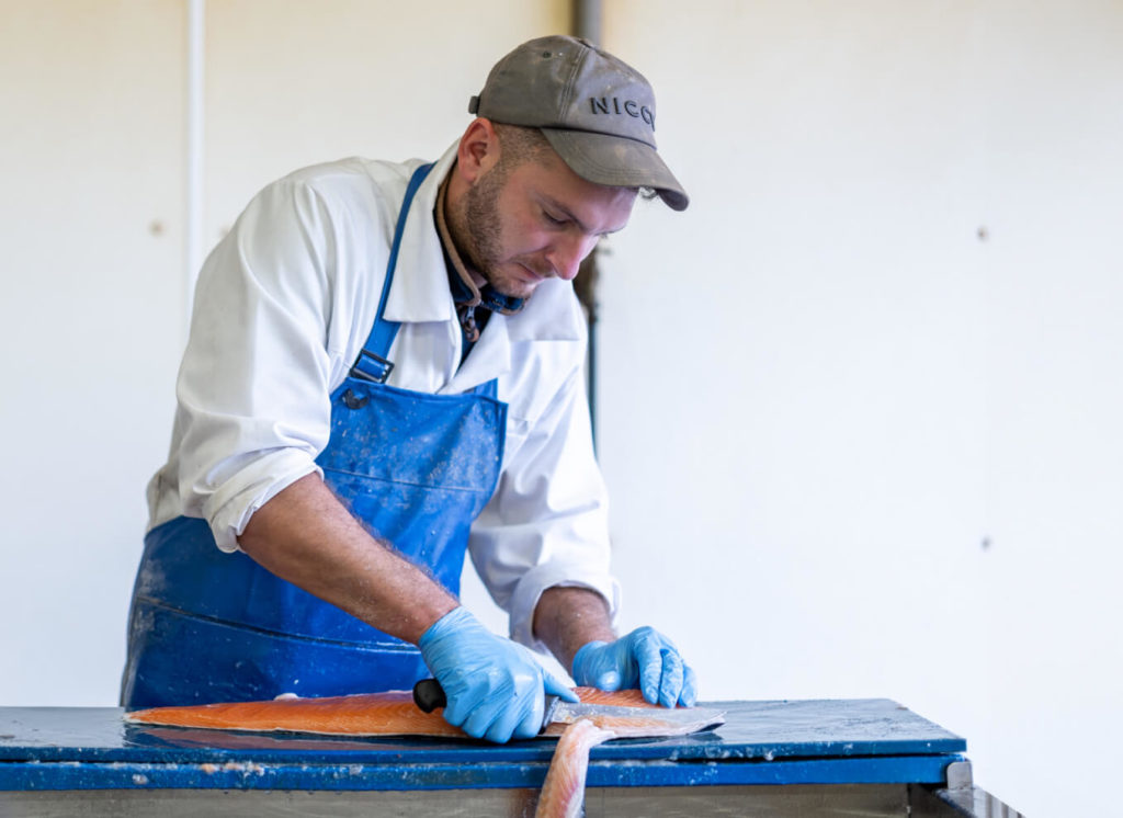 A skilled man in a blue apron is expertly slicing a fish.